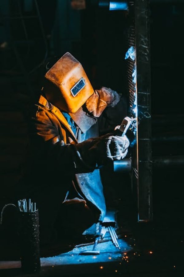 pexels-photo-2760343-2760343 A welder wearing safety gear sparks metal in a dimly lit industrial setting.